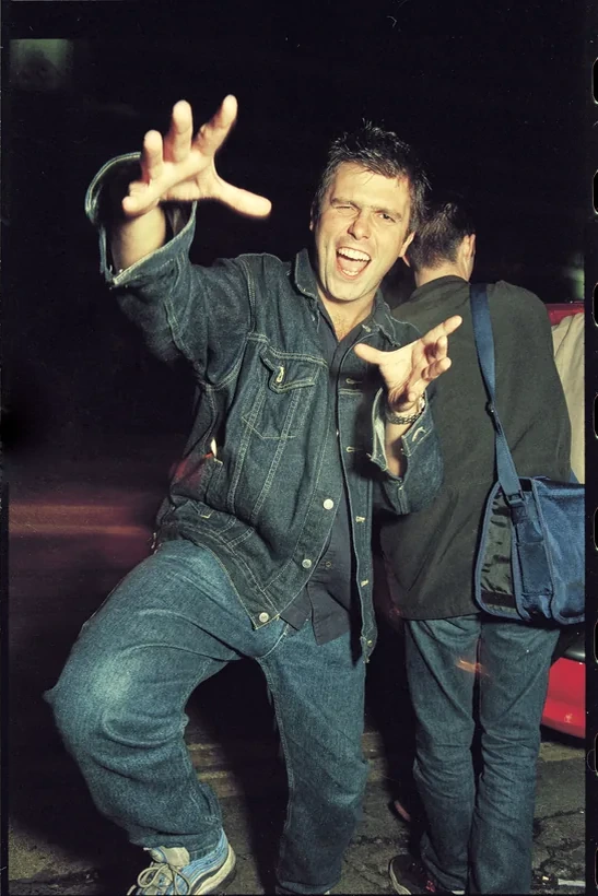Darren Emerson in a denim jacket, grinning and reaching into the flash