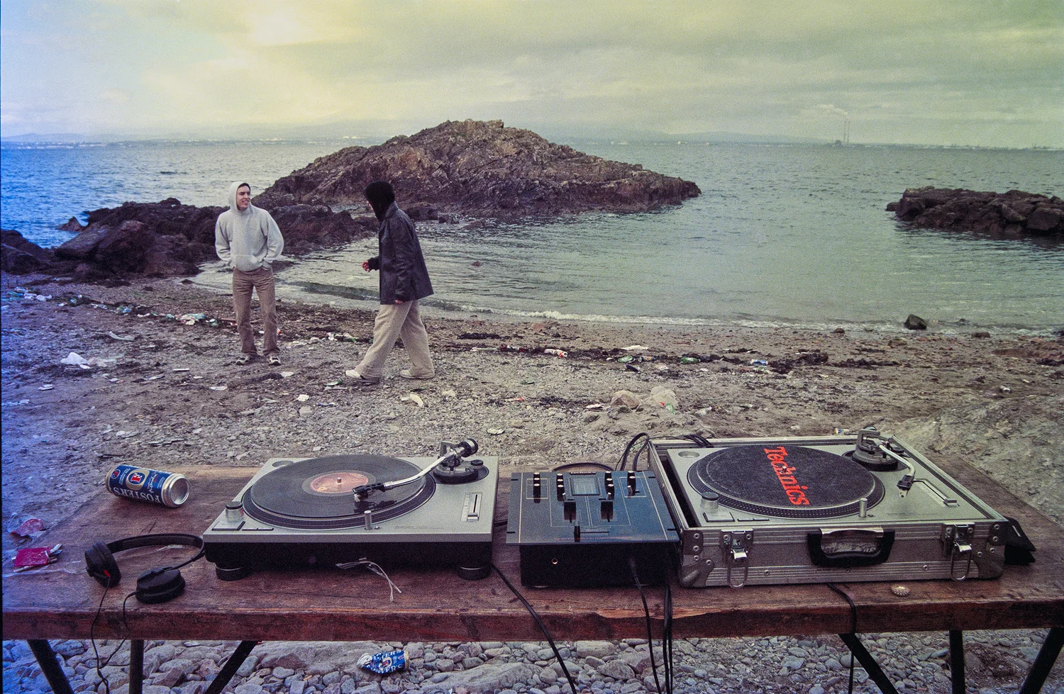 Beach Party, Sutton, Co. Dublin 1999. Two turntables and a mixer on a trestle table on the shore, the sea and rocks behind. 35mm photograph by Brendan Duffy.