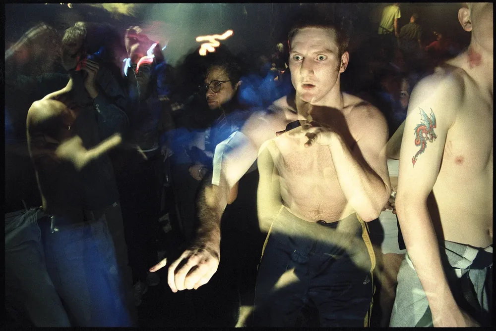 Club Oz, Dungannon, Co. Tyrone 1998. Shirtless dancers in the blur of the dancefloor, one with a dragon tattoo on the arm. 35mm photograph by Brendan Duffy.