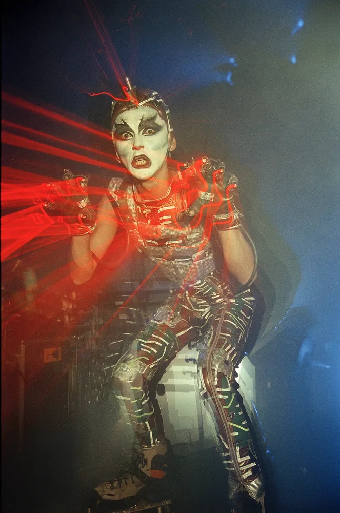 Red Box, Dublin 1998. A performer in white face paint and a silver costume crouches on stage through red laser light. 35mm photograph by Brendan Duffy.