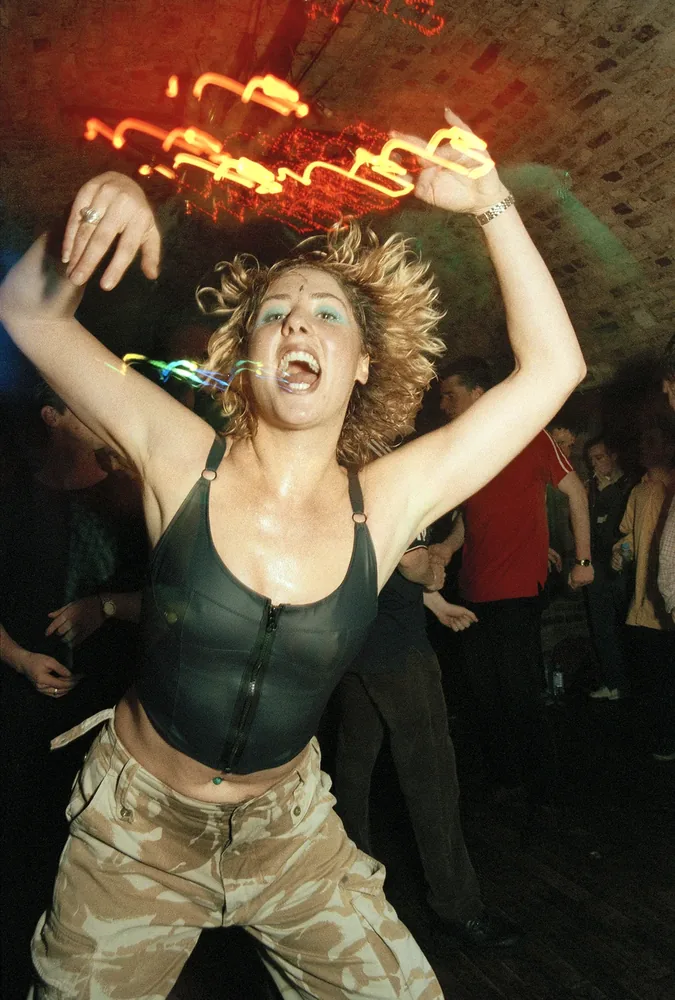 Temple Theatre, Dublin 1997. A dancer in a black leather top and camouflage trousers shouts with both arms raised, light trails overhead. 35mm photograph by Brendan Duffy.